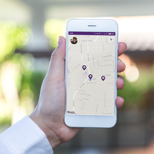 Mão segurando um celular branco cuja tela exibe o aplicativo da Loop. Na tela, há três marcadores roxos apontando no mapa o local em que há bicicletas disponíveis.